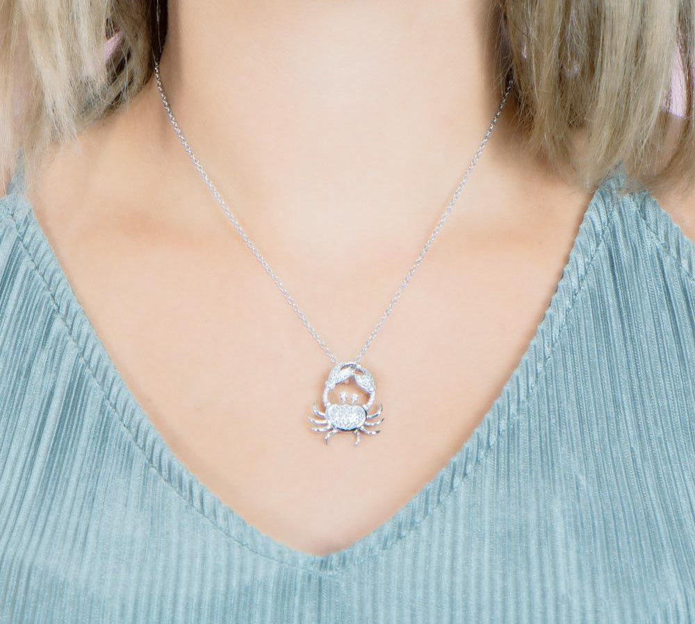 The picture shows a model weaing a 925 sterling silver, white gold plated, pavé crab pendant with topaz.