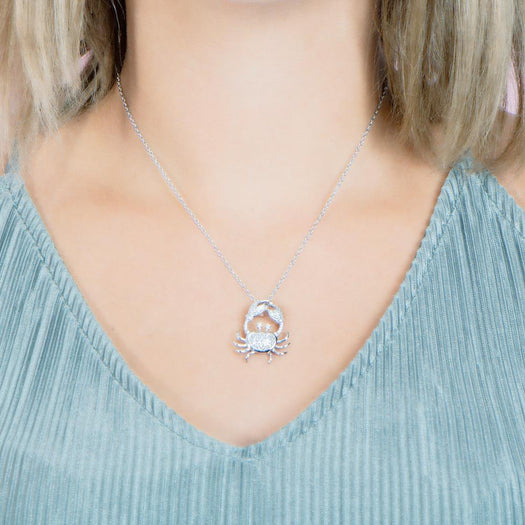 The picture shows a model weaing a 925 sterling silver, white gold plated, pavé crab pendant with topaz.