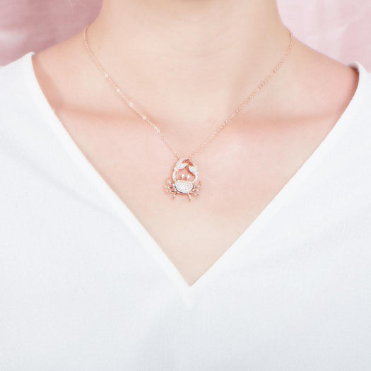 The picture shows a model wearing a 925 sterling silver, rose gold plated, pavé crab pendant with topaz.