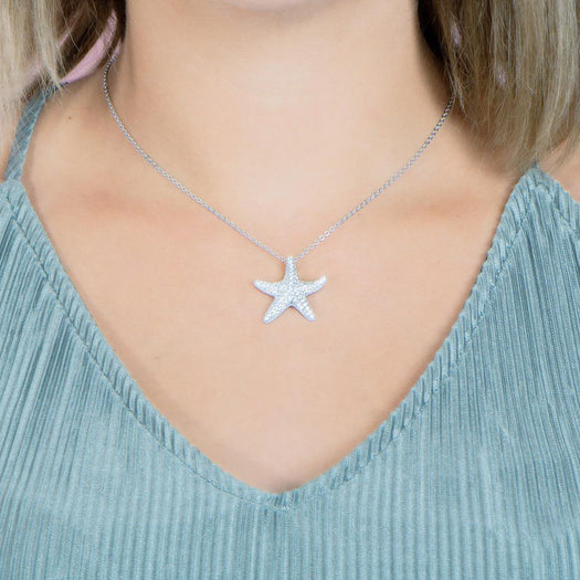 The picture shows a model wearing a 925 sterling silver, white gold plated, cushion sea star pendant with topaz.