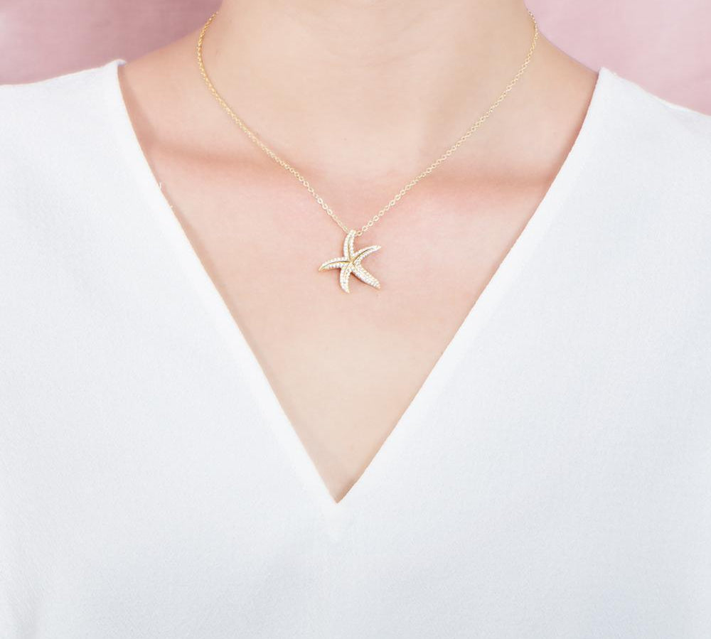 The picture shows a model wearing a 925 sterling silver, yellow gold plated, dancing starfish pendant with topaz.