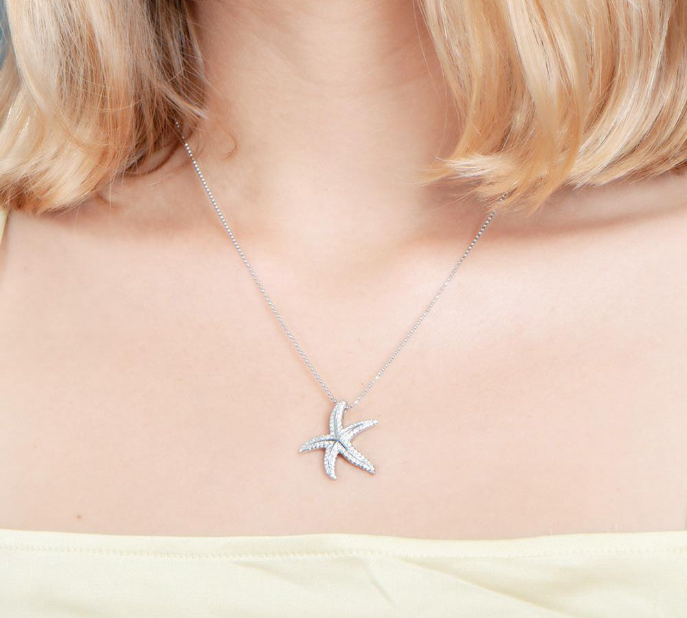 The picture shows a model wearing a 925 sterling silver, white gold plated, dancing starfish pendant with topaz.