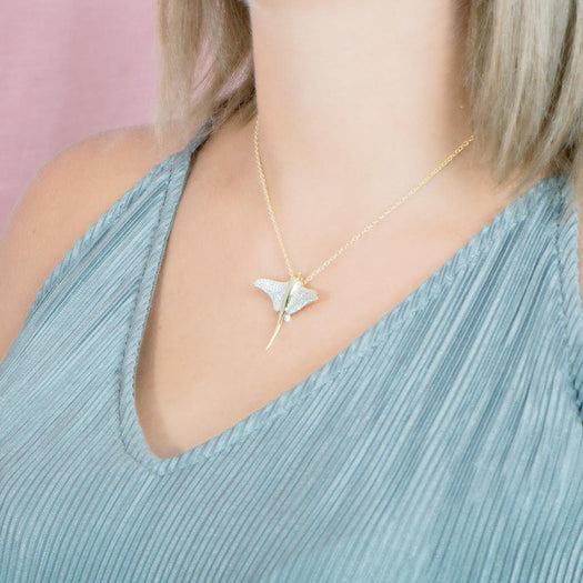 The picture shows a model wearing a 925 sterling silver, yellow gold plated, pavé eagle ray pendant with cubic zirconia.