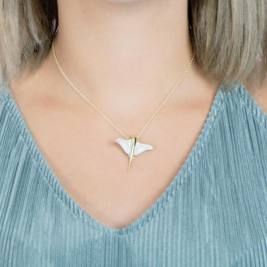 The picture shows a model wearing a 925 sterling silver, yellow gold plated, pavé eagle ray pendant with cubic zirconia.