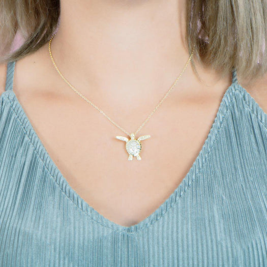 In this photo there is a model with blonde hair and a teal shirt, wearing a yellow gold sea turtle pendant with cubic zirconia.