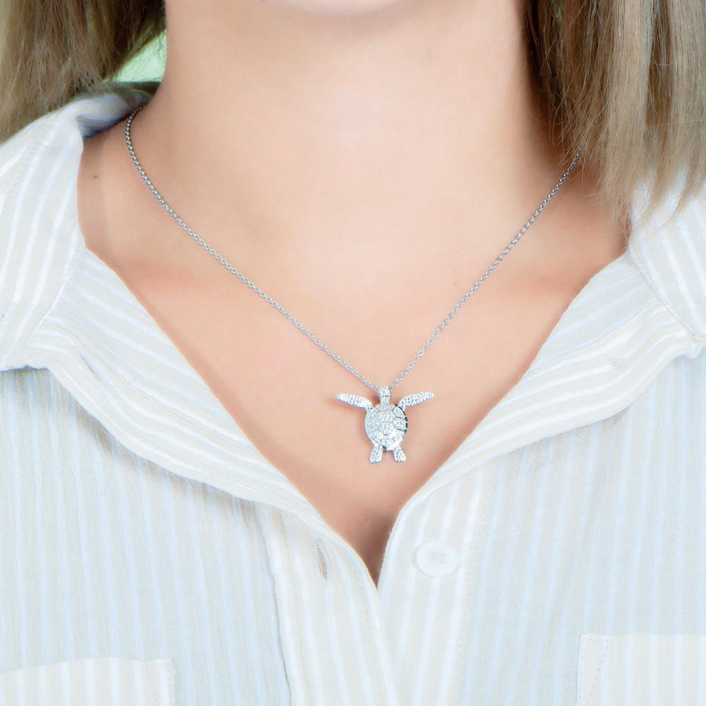 In this photo there is a model with blonde hair and a tan and white striped shirt, wearing a white gold sea turtle pendant with cubic zirconia.