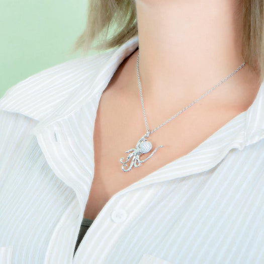 The picture shows a model wearing a 925 sterling silver, white gold vermeil, pavé octopus pendant with topaz.