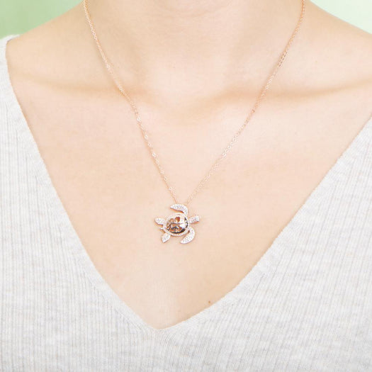 The photo shows a model wearing a rose gold pavé hibiscus adorned sea turtle pendant.