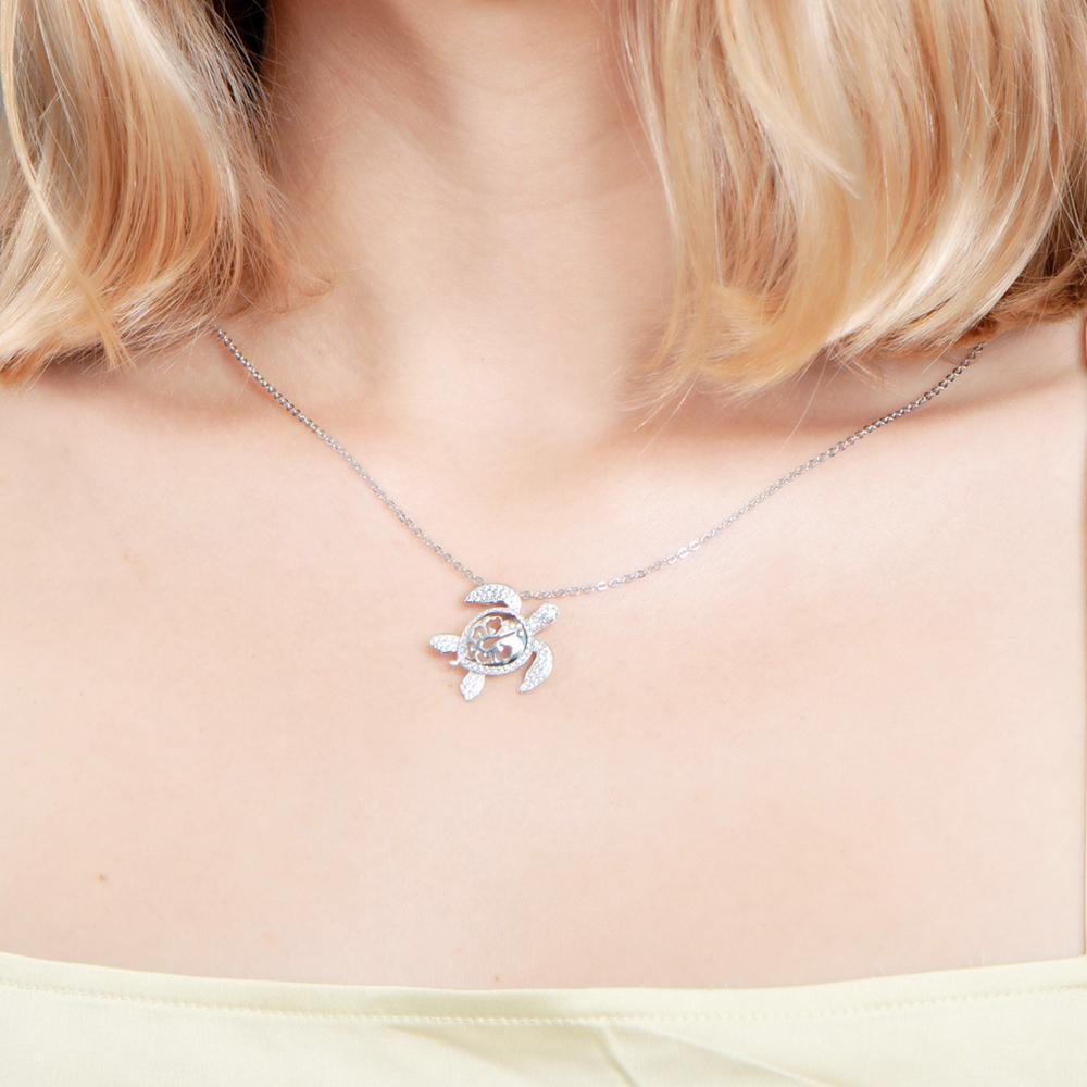 The photo shows a model wearing a white gold pavé hibiscus adorned sea turtle pendant.
