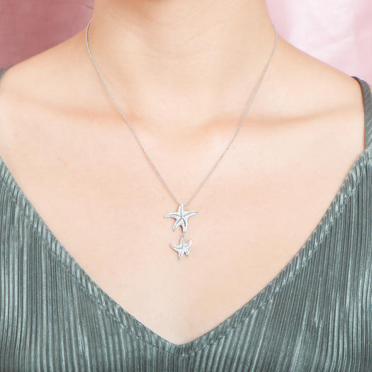 The picture shows a model wearing a 925 sterling silver, white gold vermeil, hanging double starfish pendant with topaz.