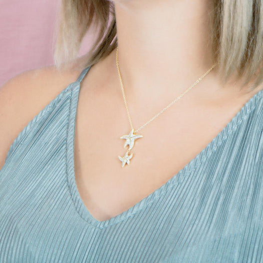 The picture shows a model wearing a 925 sterling silver, yellow gold vermeil, hanging double starfish pendant with topaz.