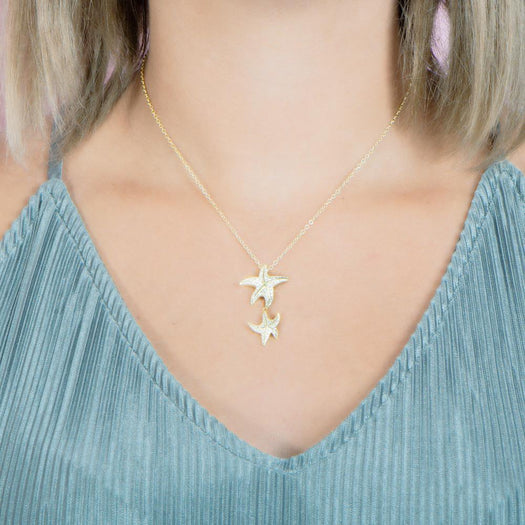 The picture shows a model wearing a 925 sterling silver, yellow gold vermeil, hanging double starfish pendant with topaz.