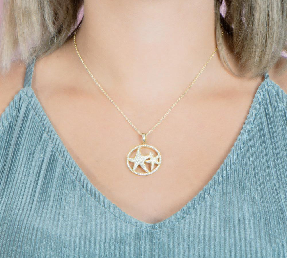 The picture shows a model wearing a 925 sterling silver, yellow gold vermeil, double starfish circle pendant with topaz.