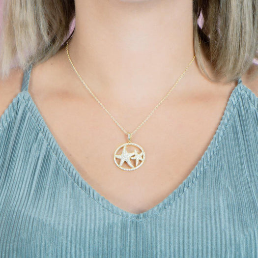 The picture shows a model wearing a 925 sterling silver, yellow gold vermeil, double starfish circle pendant with topaz.
