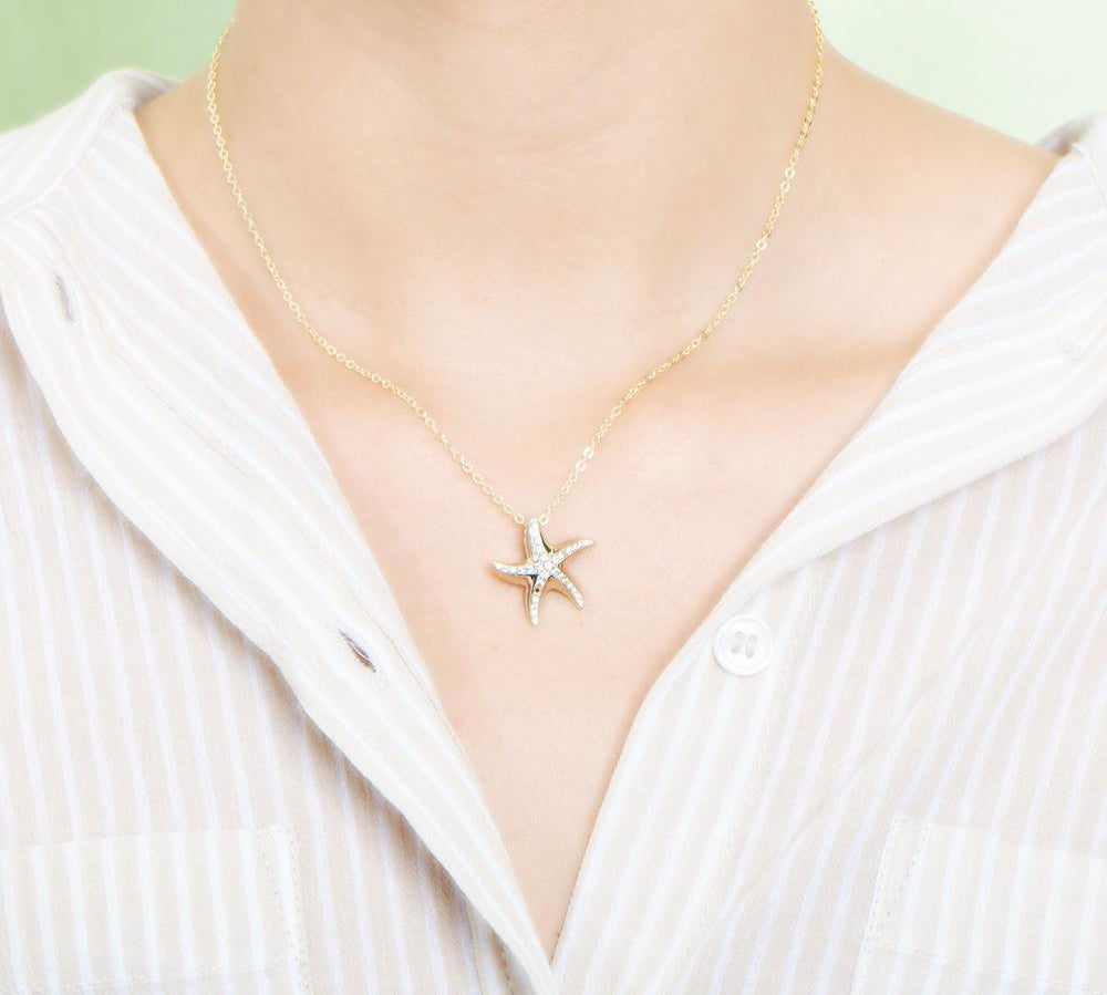 The picture shows a model wearing a 925 sterling silver, yellow gold vermeil, starfish pendant with topaz.