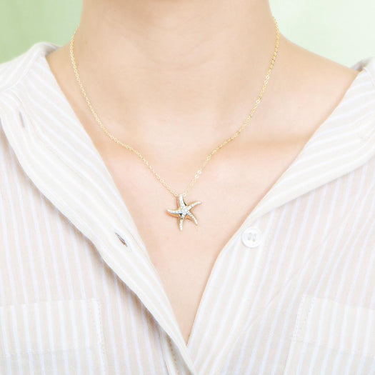 The picture shows a model wearing a 925 sterling silver, yellow gold vermeil, starfish pendant with topaz.