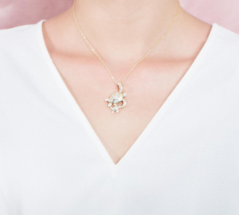 The picture shows a model wearing a 925 sterling silver, yellow gold vermeil, double sea turtle pendant with topaz.