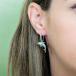 The picture shows a model wearing a 925 sterling silver dolphin earring with topaz and sapphire.