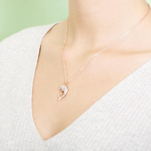 The picture shows a model wearing a 925 sterling silver, rose gold-vermeil, dolphin pendant with cubic zirconia.