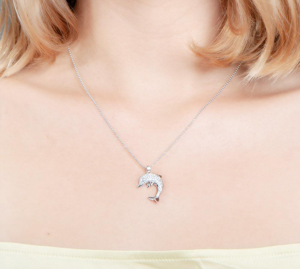 The picture shows a model wearing a 925 sterling silver, white gold-vermeil, dolphin pendant with cubic zirconia.