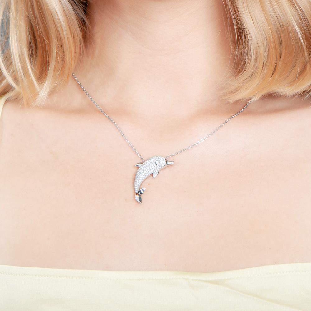 The picture shows a model wearing a 925 sterling silver, white gold-vermeil, dolphin pendant with topaz.