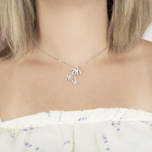 In this photo there is a model with blonde hair and a white shirt with purple flowers, wearing a white gold double palm tree pendant with topaz gemstones.