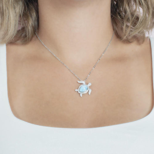 The picture shows a model wearing a 925 sterling silver pavé larimar sea turtle pendant with cubic zirconia.