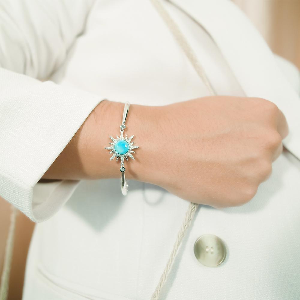 In this photo there is a model wearing a 925 sterling silver sun bracelet with blue larimar, topaz, and aquamarine gemstones.