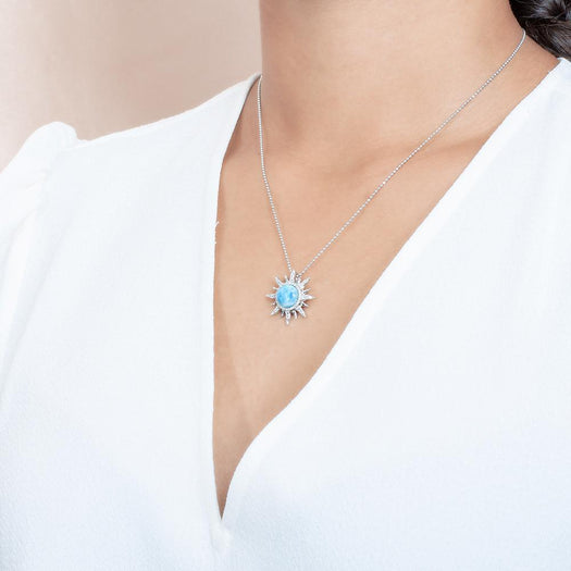 In this photo there is a model with brown hair and a white shirt turned to the left, wearing a sterling silver sun pendant with topaz and one blue larimar gemstone.