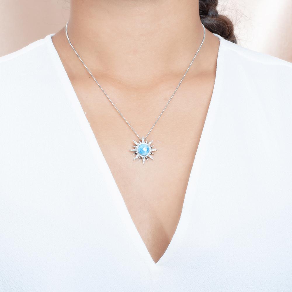 In this photo there is a model with brown hair and a white shirt, wearing a sterling silver sun pendant with topaz and one blue larimar gemstone.