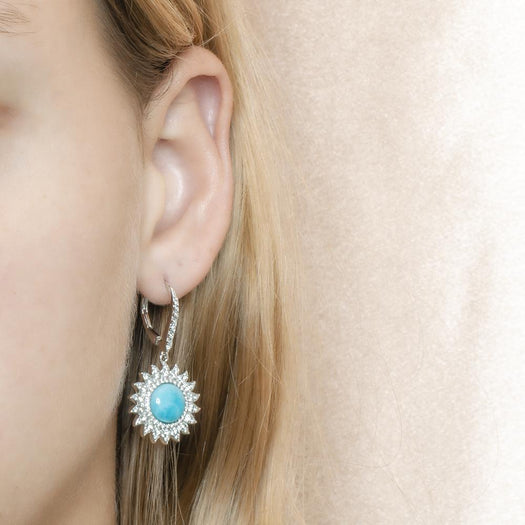 In this photo is a model with blonde hair wearing sterling silver sunflower dangle earrings with blue larimar and topaz gemstones.