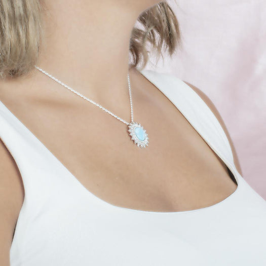 In this photo there is a model turned to the right with blonde hair and a white shirt, wearing a sterling silver sunflower pendant with topaz and one blue larimar gemstone.
