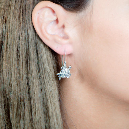 The picture shows a model wearing a 925 sterling silver sea turtle hook earring with topaz.