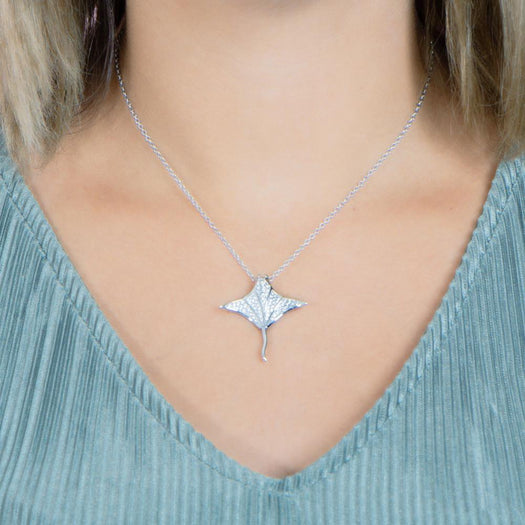 The picture shows a model wearing a 925 sterling silver, white gold vermeil, pavé manta ray pendant with topaz.