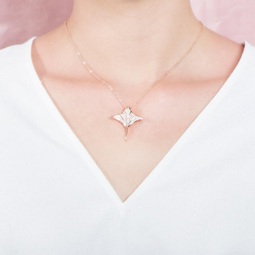 The picture shows a model wearing a 925 sterling silver, rose gold vermeil, pavé manta ray pendant with topaz.