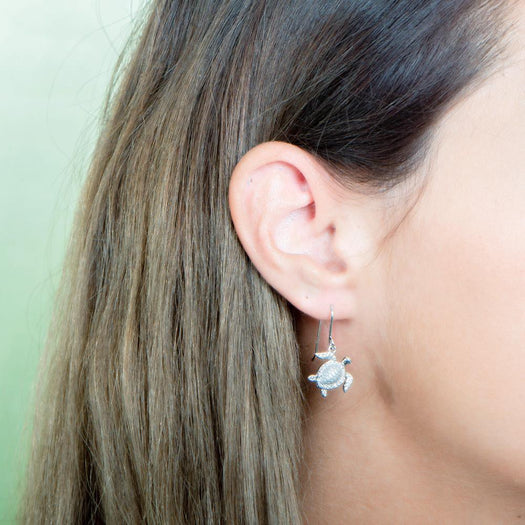 The picture shows a model wearing a 925 sterling silver white gold-vermeil sea turtle hook earring with topaz.