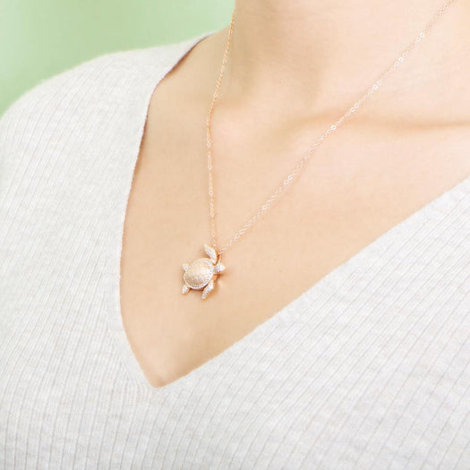 The picture shows a model wearing a 925 sterling silver, rose gold plated, sea turtle pendant with topaz.