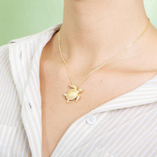 The picture shows a model wearing a 925 sterling silver, yellow gold plated, sea turtle pendant with topaz.