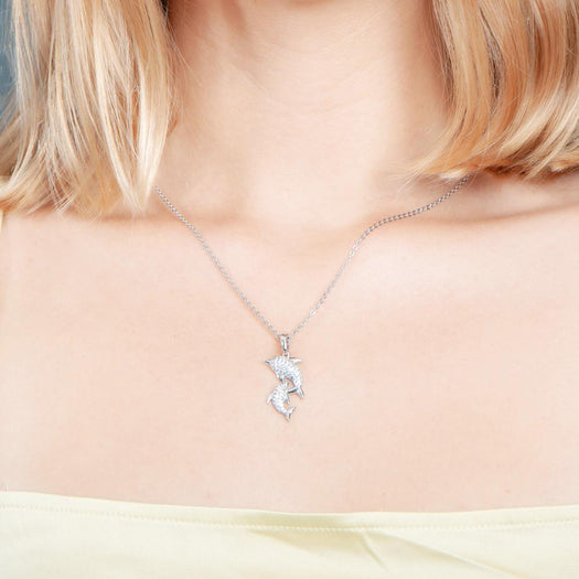 The picture shows a model wearing a 925 sterling silver, white gold vermeil, two dolphin pendant with topaz.