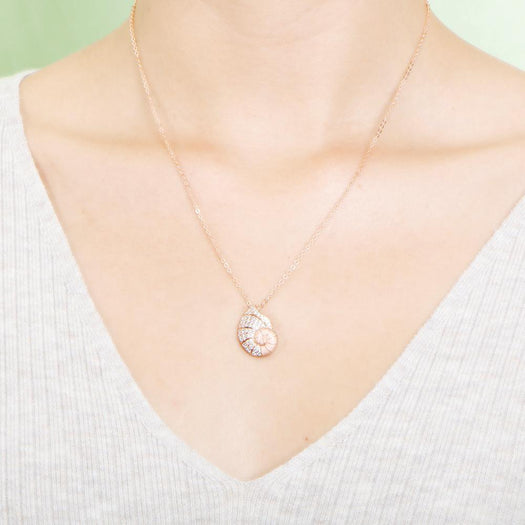 The picture shows a model wearing a 925 sterling silver, rose gold vermeil, pavé nautilus pendant with topaz.