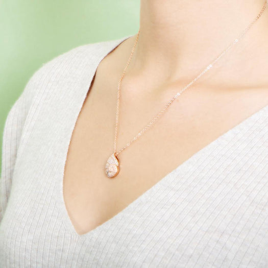 The picture shows a model wearing a 925 sterling silver, rose gold vermeil, pavé nautilus pendant with topaz.