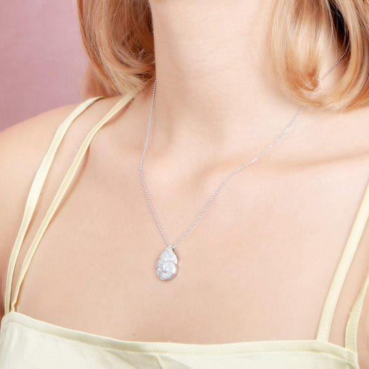 The picture shows a model wearing a 925 sterling silver, white gold vermeil, pavé nautilus pendant with topaz.