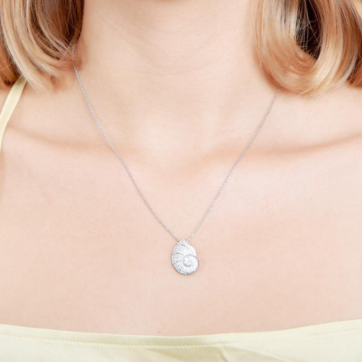 The picture shows a model wearing a 925 sterling silver, white gold vermeil, pavé nautilus pendant with topaz.