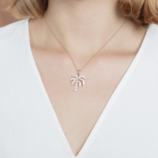 In this photo there is a model with blonde hair and a white shirt, wearing a rose gold palm tree pendant with topaz gemstones.