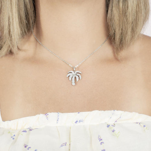 In this photo there is a model with blonde hair and a white shirt with flowers, wearing a white gold palm tree pendant with topaz gemstones.
