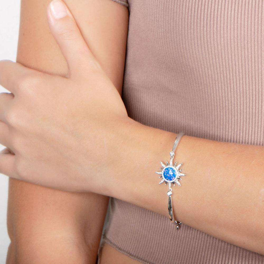 In this photo there is a close-up of a model with a beige shirt, wearing a sterling silver sun bracelet with aquamarine, topaz, and one blue opalite gemstone on her left wrist.