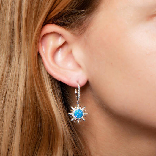 In this photo there is a close-up of a model with blonde hair wearing sterling silver sun earrings with blue opalite gemstones and topaz.
