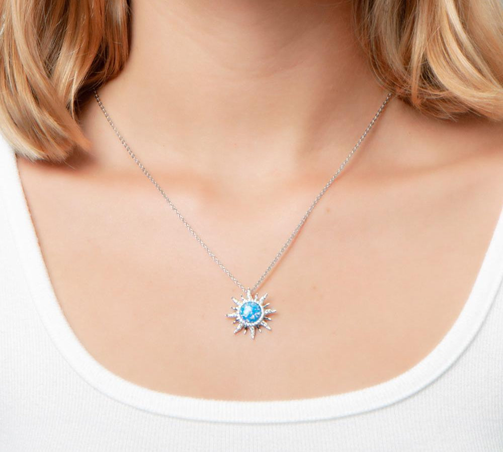 In this photo there is a model with blonde hair and a white shirt, wearing a sterling silver sun pendant with topaz and blue opalite gemstones.