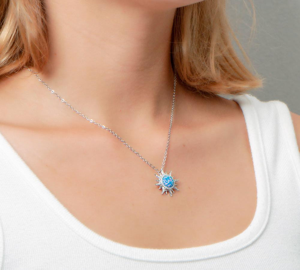 In this photo there is a model turned to the right with blonde hair and a white shirt, wearing a sterling silver sun pendant with topaz and blue opalite gemstones.