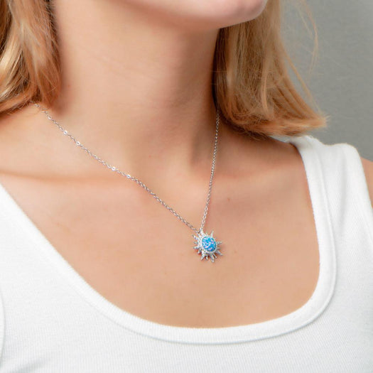 In this photo there is a model turned to the right with blonde hair and a white shirt, wearing a sterling silver sun pendant with topaz and blue opalite gemstones.